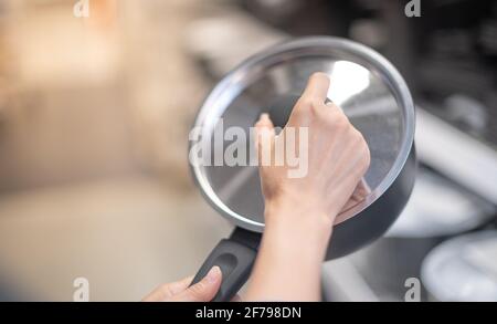 Mano femmina che tiene nuova pentola vuota da cucina coperta con coperchio in vetro trasparente. Foto Stock