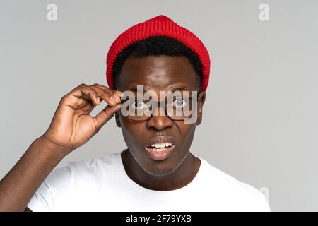 Uomo afro-americano incerto dubbio in cappello rosso che tiene occhiali, pari, guardando sospettoso la macchina fotografica Foto Stock