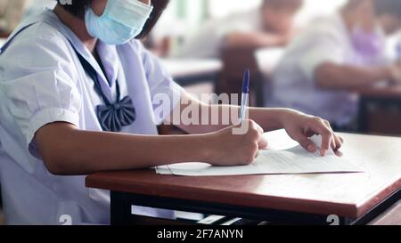 Gli studenti che stanno prendendo l'esame e scrivendo la risposta in classe con Wear Face mack. Concetto di test di formazione Foto Stock