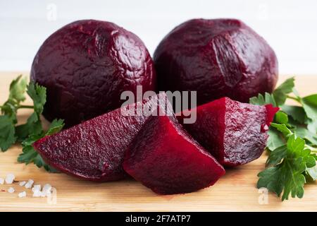 Barbabietole bollite intere e tagliate su un tagliere con foglie di prezzemolo su fondo bianco. Spazio di copia, Foto Stock