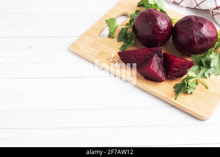 Barbabietole bollite intere e tagliate su un tagliere con foglie di prezzemolo su fondo bianco. Spazio di copia, Foto Stock