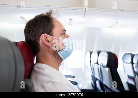 Uomo su un aereo che indossa una maschera chirurgica che viaggia durante La pandemia del coronavirus COVID-19 Foto Stock