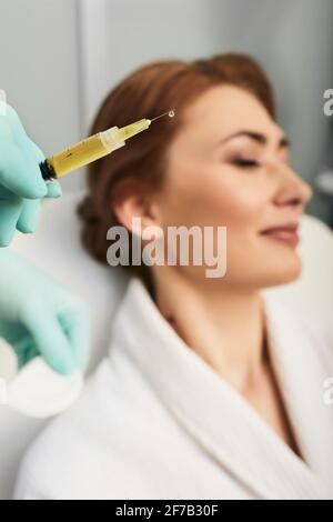 Siringa con plasma sanguigno di un paziente in una mano di un cosmetologo per un plasmolifting della pelle del viso di una donna. Plasma terapia, il ripristino delle cellule della pelle Foto Stock