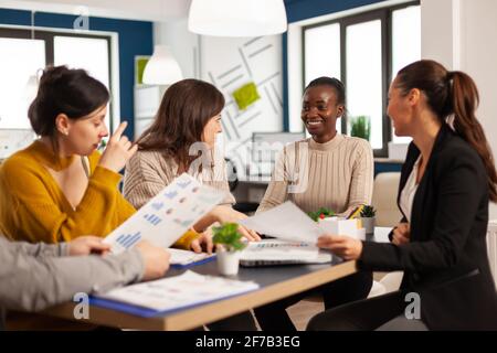 Le donne impegnate in attività multiculturali analizzano le statistiche finanziarie annuali che si trovano alla scrivania e che tengono documenti che cercano soluzioni aziendali. Team di imprenditori che lavorano in azienda, brainstorming Foto Stock