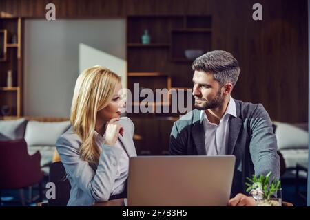 Una coppia d'affari si siede in un caffè e ha una conversazione di lavoro. C'è un computer portatile su un tavolo. Incontri d'affari, tecnologia, cooperazione Foto Stock