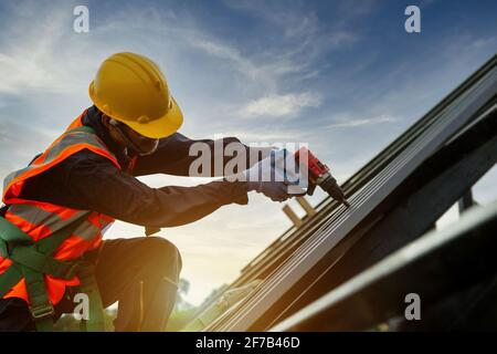 Tecnico Roofer lavoratore in uniforme di protezione indossare e guanti, cantiere installare nuovo tetto, attrezzi per tetti, trapano elettrico utilizzato su nuovi tetti wi Foto Stock