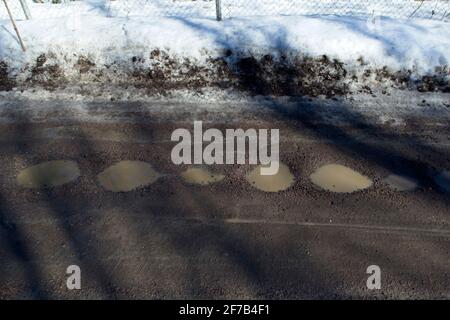 strada sterrata con pozzanghere quando la neve inizia a sciogliersi Foto Stock