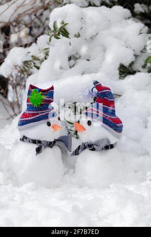 Due simpatici pupazzi di neve in una scena invernale innevata si sono accoccolati insieme. Vestiti con cappelli e sciarpe e naso di carota che si guardano l'un l'altro. Vacanze di Natale Foto Stock