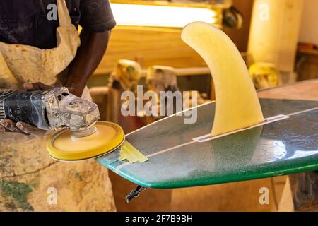 Primo piano di un artigiano africano tavola da surf Shaper lavorare in un'officina di riparazione Foto Stock