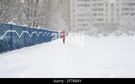 Una donna cammina lungo una recinzione verso un edificio a più piani durante una nevicata a Mosca, Russia Foto Stock