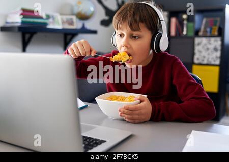 Ragazzo che mangia la colazione durante le lezioni online Foto Stock