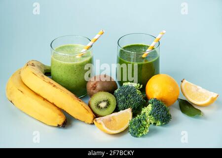 Due frullati verdi e ingredienti: Banana, kiwi, broccoli, limone su sfondo blu, primo piano. Concetto sano di cibo vegano crudo. Messa a fuoco selettiva. Foto Stock