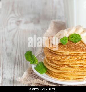 Pancake serviti con latte, guarniti con foglie di menta e fette di banana. Versare con miele o sciroppo d'acero. Foto Stock