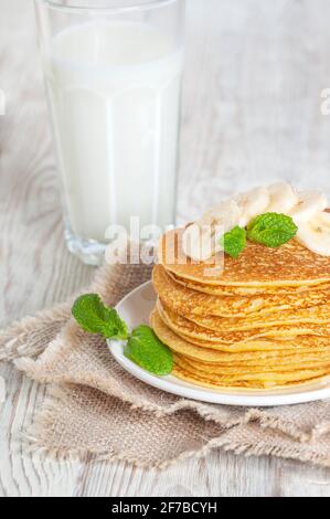 Pancake serviti con latte, guarniti con foglie di menta e fette di banana. Versare con miele o sciroppo d'acero. Foto Stock