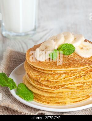 Pancake serviti con latte, guarniti con foglie di menta e fette di banana. Versare con miele o sciroppo d'acero. Foto Stock