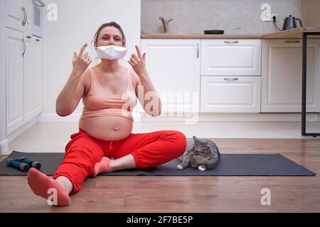 Sport a casa durante la gravidanza durante la quarantena a causa di influenza Donna incinta virus su allenamento fitness con maschera medica viso Foto Stock