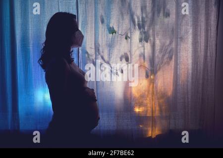 Silhouette di una donna incinta con una maschera medica viso. Problemi di gravidanza e la pandemia del coronavirus Foto Stock