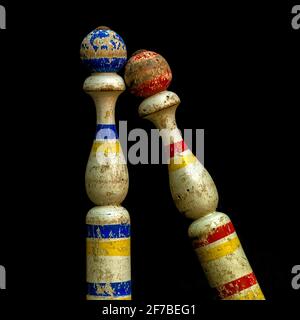 Due birilli in legno con marcature colorate che si appoggiano l'uno contro l'altro sotto un'illuminazione soffusa in un ambiente interno Foto Stock