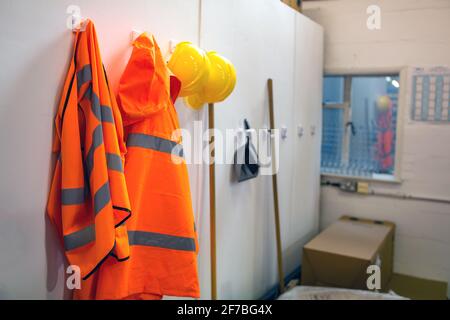 Indumenti di protezione ad alta visibilità e cappelli rigidi appesi in un magazzino per un facile accesso ai lavoratori. Magazzino, negozi, concetto di equipaggiamento di sicurezza Foto Stock