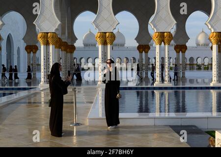 I turisti che ammirano il bacino d'acqua e i portici della Moschea Sheikh Zayed ad Abu Dhabi, Emirati Arabi Uniti. Foto Stock