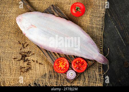 Pesce sogliola fresco crudo con pomodori su un tagliere di legno. Pancia bianca di un pesce Foto Stock