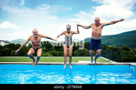 Gruppo di anziani allegri in piscina all'aperto in cortile, saltando. Foto Stock