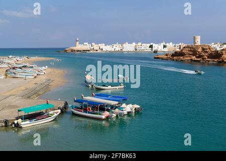 Barche turistiche e barche da pesca sulla spiaggia della città sur. Sul lato destro il villaggio Aylah con faro e torre di guardia. Oman. Foto Stock