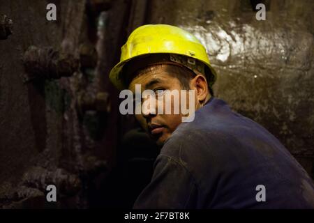 Stepnogorsk, Kazakhstan - 04 aprile 2012: Giovane tecnico asiatico in casco da lavoro giallo. Posa su fondo di metallo arrugginito marrone. Foto Stock