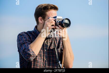 Reporter scatta foto. Impostazioni manuali. Blogger di viaggio. Attrezzatura d'epoca. Fotografo hipster. Blogger tiro vlog. Ragazzo all'aperto cielo blu Foto Stock