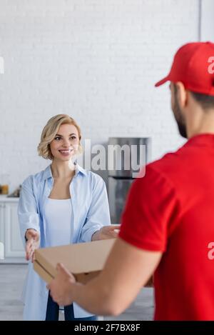 gioiosa donna bionda che prende le scatole della pizza dal corriere arabo sul primo piano offuscato Foto Stock