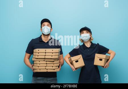 corrieri interrazziali in maschere mediche guardando in su mentre tiene i pacchetti su blu Foto Stock