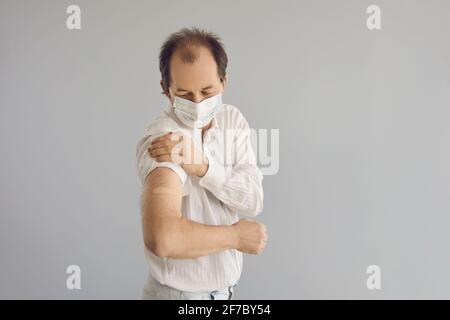 L'uomo maturo in una maschera medica mostra il suo braccio Dopo aver ottenuto un vaccino Covid 19 Foto Stock