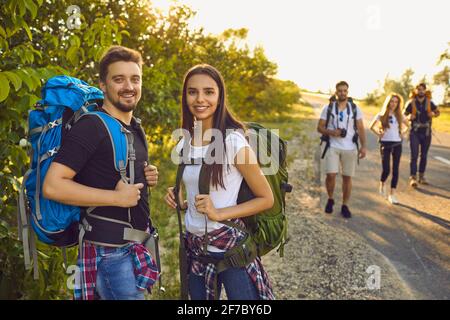 Coppia escursionista con zaini in natura. Un gruppo di amici sta camminando lungo la strada in campagna. Foto Stock