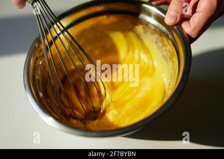 Lo chef mescola zucchero e uova in una ciotola di metallo utilizzando una frusta a filo. Torte fatte in casa, preparazione torta di Pasqua o gustoso concetto di biscotti. Foto di alta qualità Foto Stock