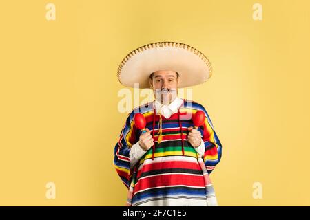 Uomo felice in sombrero e poncho luminoso isolato sopra il giallo sfondo Foto Stock