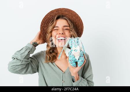 Bella ragazza bionda felice che indossa cappello di paglia e blusa verde mostrando il suo coniglio giocattolo mentre si trova su sfondo bianco studio. Foto Stock