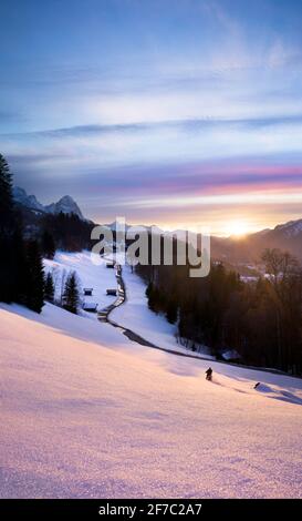 Splendido tramonto rosa in montagna con strada di prima linea verso chiesa e motociclista divertirsi nella neve fresca Foto Stock