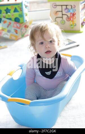 kleines Mädchen sitzt in einer blauen Plastikwäschewanne - bambina seduta nella vasca di plastica blu della lavanderia Foto Stock