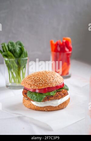 Hamburger vegano con fagioli rossi, pepe rosso, spinaci, yogurt bianco e foglie di insalata fresca e verdure tagliate sullo sfondo. Foto Stock