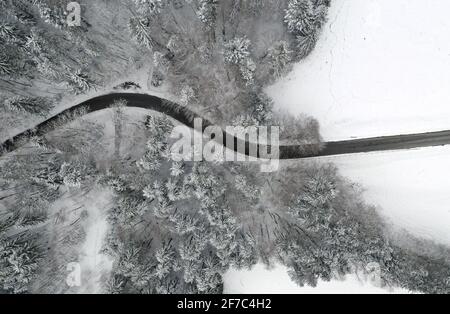 Bernbeuren, Germania. 06 Aprile 2021. Una strada attraversa una foresta coperta di neve (vista aerea con un drone). Credit: Karl-Josef Hildenbrand/dpa/Alamy Live News Foto Stock
