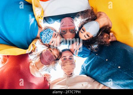 Gruppo multirazziale di amici che indossano maschere facciali protettive che prendono un Selfie - nuovo concetto di amicizia normale con i giovani alla ricerca verso il basso alla telecamera an Foto Stock