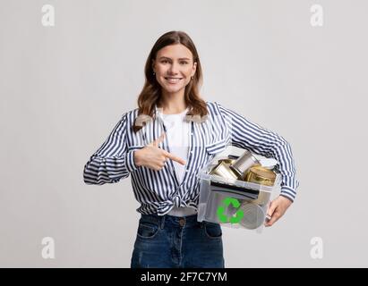 Riciclo del metallo. Contenitore in plastica con contenitore in plastica Millennial Lady positivo con lattine in alluminio Foto Stock