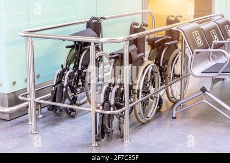 Sedie a rotelle ripiegate in un luogo pubblico nell'edificio del terminal dell'aeroporto, assistenza a persone con mobilità limitata Foto Stock