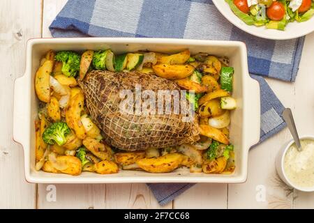 Piatto da forno con involtini di maiale arrosto, patate e verdure, serve con salsa e insalata Foto Stock