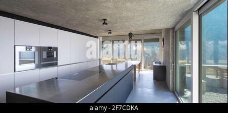 Moderna cucina bianca con grande isola, piano cottura a induzione, due  forni, lavello e piano in acciaio inox. Grandi finestre che si affacciano  sulla natura della Svizzera. N Foto stock - Alamy