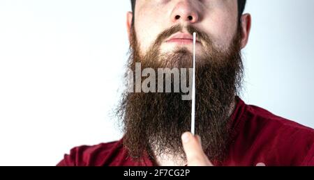 Test automatico del coronavirus a casa. Giovane uomo esegue un test rapido covid-19 a casa. Test con bastoncino di cotone nel naso del giovane uomo su bianco Foto Stock