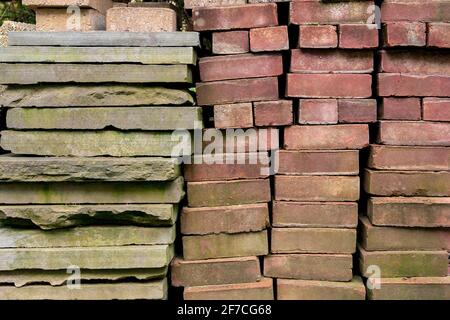 Blocchi di mattoni, lastre di ardesia e altri materiali da costruzione sono visti impilati all'inizio della primavera di aprile giorno in moody, astratta, grunge immagine di sfondo Foto Stock