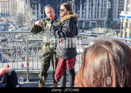 KIEV, UCRAINA - 13 MARZO 2014: Jared Leto è fotografato con l'esercito ucraino contro un edificio bruciato e un campo tenda Foto Stock