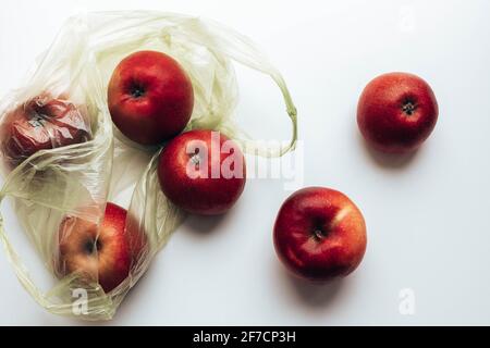 Mele rosse fresche in sacchetto di plastica verde su sfondo grigio. Foto Stock