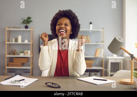 Felice lavoratore d'ufficio di affari che sente l'eccitamento che alza il pugno siedono a. scrivania Foto Stock